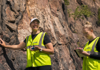 Next to the rock, two people wearing safety vests.