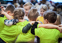 A group of children wearing bright green shirts. The children have gathered together and have their arms around each other.