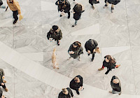 An overhead shot of people walking on a light stone floor.