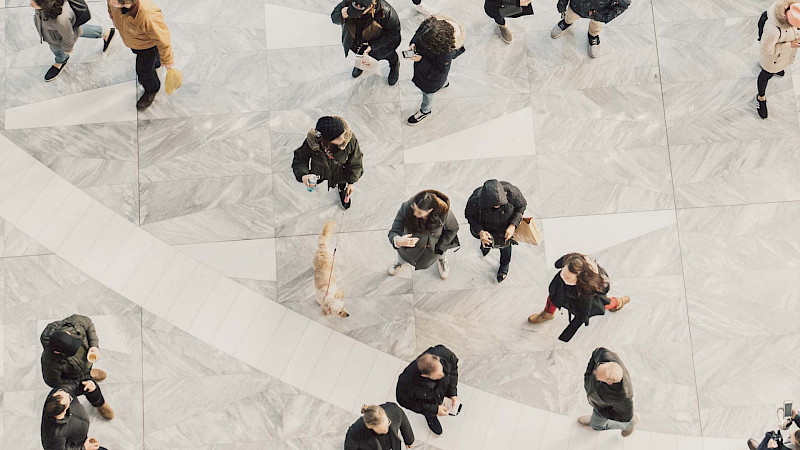 Ylhäältäpäin otettu kuva ihmisistä kävelemässä vaalealla kivilattialla.