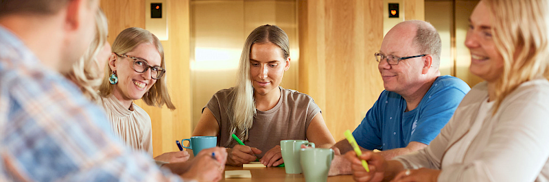 Kuvituskuva. Useita ihmisiä istumassa ja keskustelemassa pöydän ympärillä toimistossa.