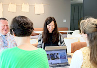 Illustration. Several people sit around the table in the meeting room to discuss. There is an open computer screen on the table.