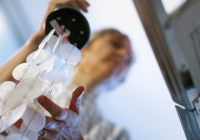 The person is holding a lamp-like object made of white circles. Light transparent circular patterns hang from the object. A person holds an object by its black base. In the background is a blurry picture of a room with a window.