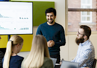 A group of people in a meeting with a presentation on the screen in the background.