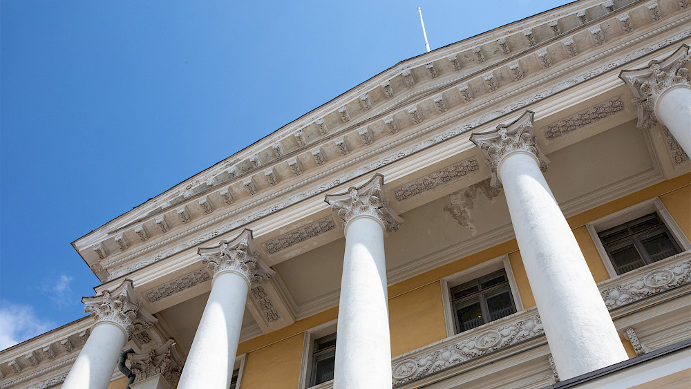 Närbild av statsrådets slott. Bilden visar massiva pelare och takdekorationer. Himlen är blå.